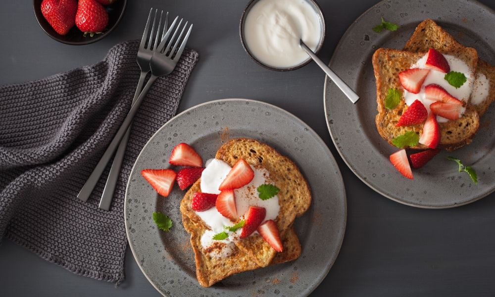 Two slices of toasted bread topped with yogurt, sliced strawberries, and mint leaves.