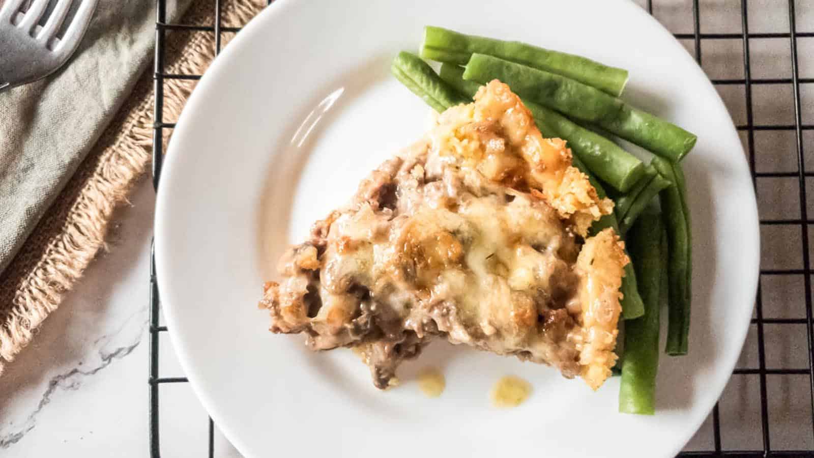 A slice of meat pie on a plate with green beans.