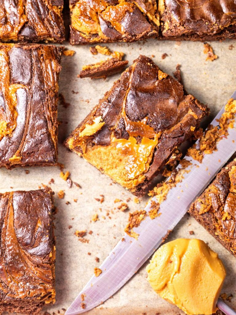 Close-up of sliced peanut butter brownies with caramel swirl on parchment paper.