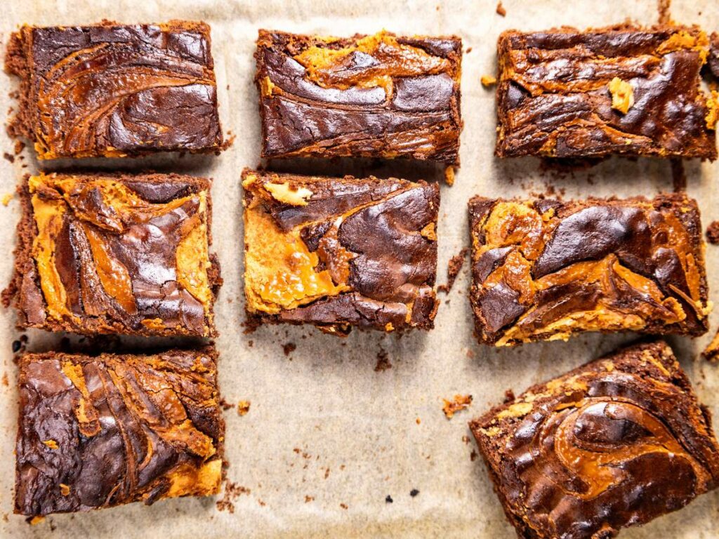 Nine chocolate and peanut butter swirl brownies on parchment paper.