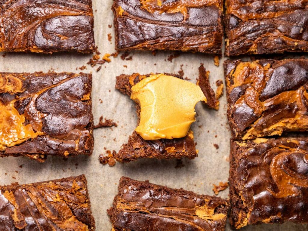 Peanut butter brownies with swirled patterns are arranged on parchment.