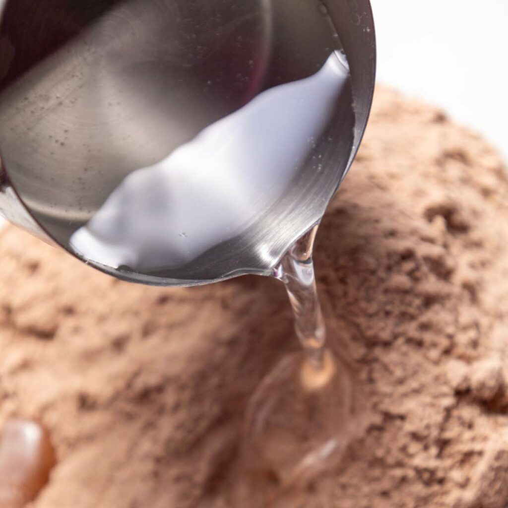 Water being poured from a metal cup into a mound of brown powder.