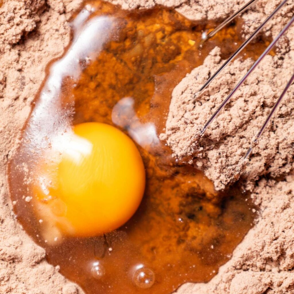 Egg yolk and egg whites on cocoa powder, next to a whisk.