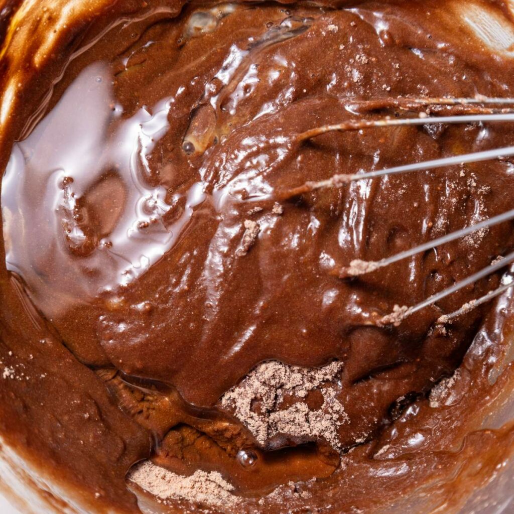 Close-up of a whisk mixing chocolate cake batter in a bowl.