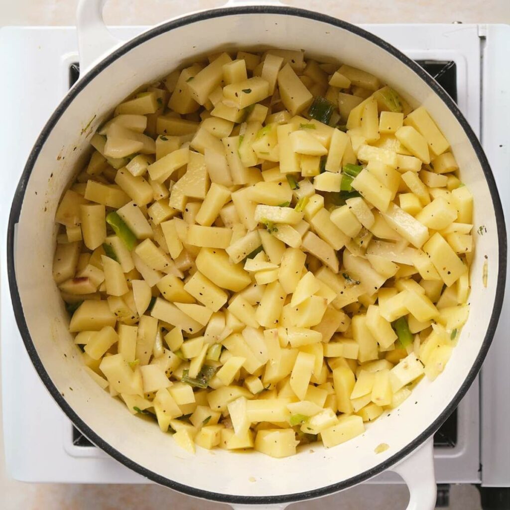 Chopped potatoes and herbs cooking in a white pot on a stove.