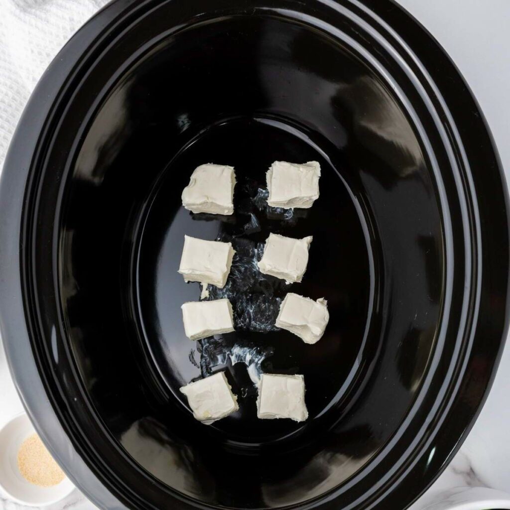 Blocks of cream cheese are arranged in a black slow cooker.