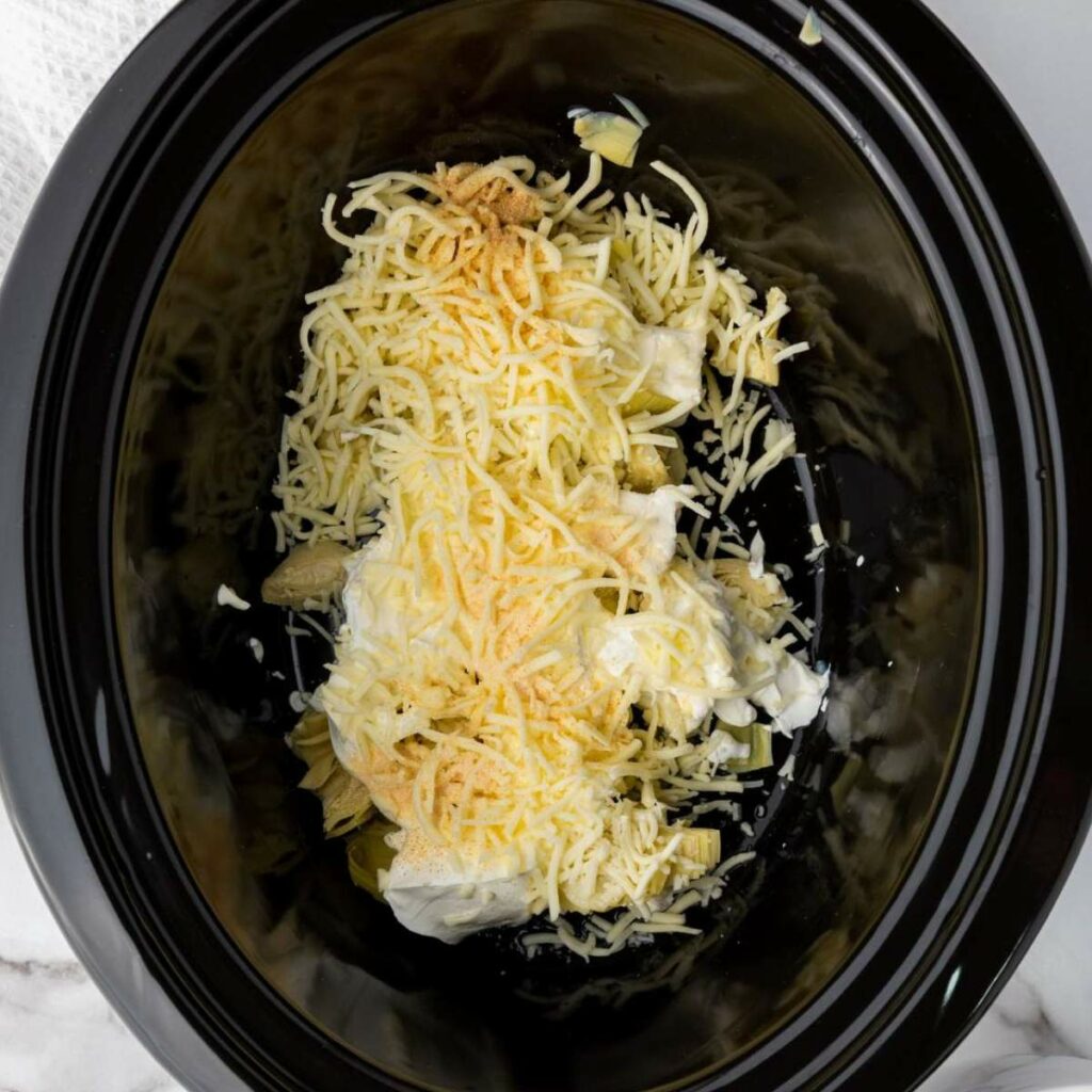 Shredded cheese and cream ingredients in a black slow cooker.