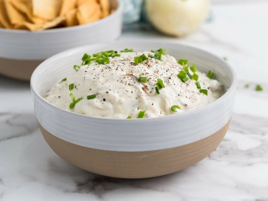 A bowl of caramelized onion dip topped with chopped green onions and black pepper.