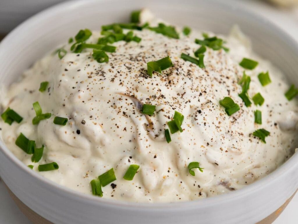 A bowl of creamy caramelized onion dip topped with chopped green onions and black pepper.