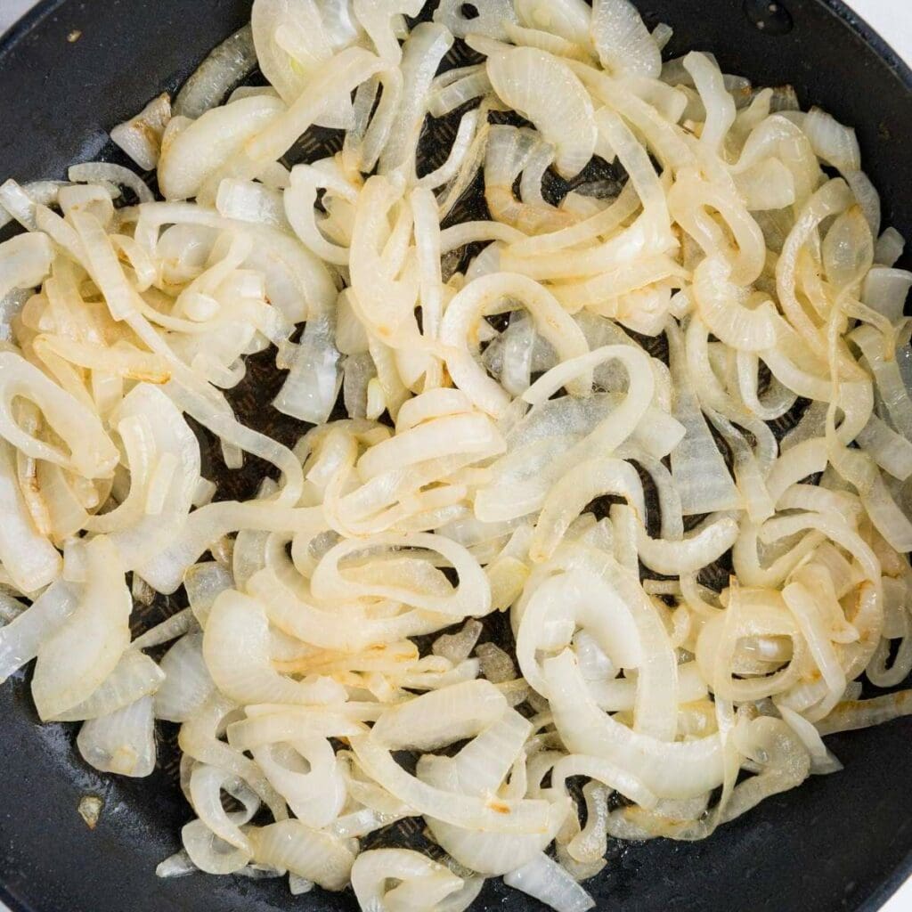 Sliced onions sautéing in a pan until translucent, showing slight browning.