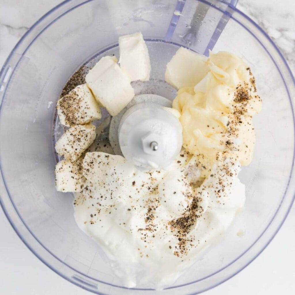 Ingredients in a food processor: cubed butter, mayonnaise, sour cream, and ground pepper.