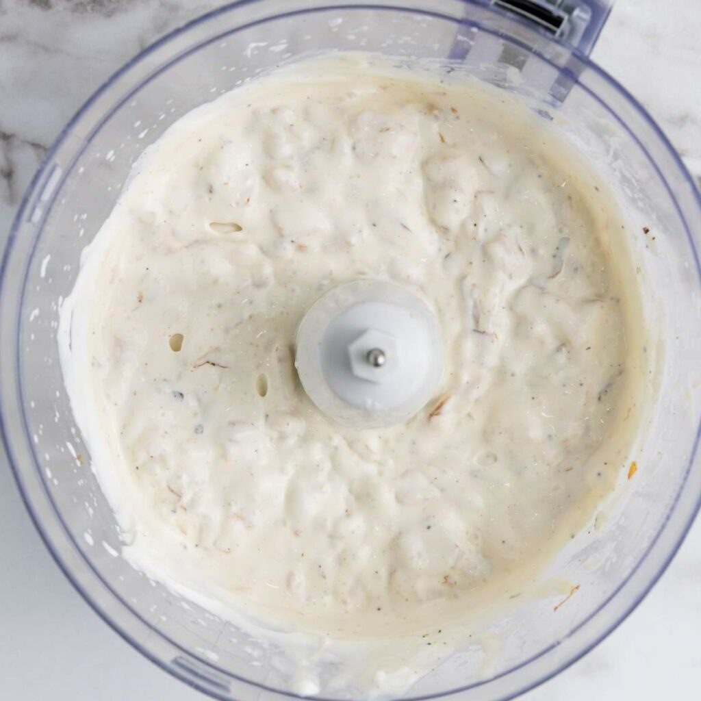 A creamy mixture inside a food processor, viewed from above.