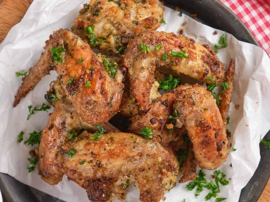 A plate of parmesan and garlic wings garnished with chopped parsley on parchment paper.