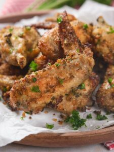 A plate of crispy parmesan and garlic wings garnished with chopped parsley on a sheet of parchment paper.