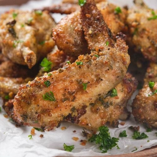 A plate of crispy parmesan and garlic wings garnished with chopped parsley on a sheet of parchment paper.