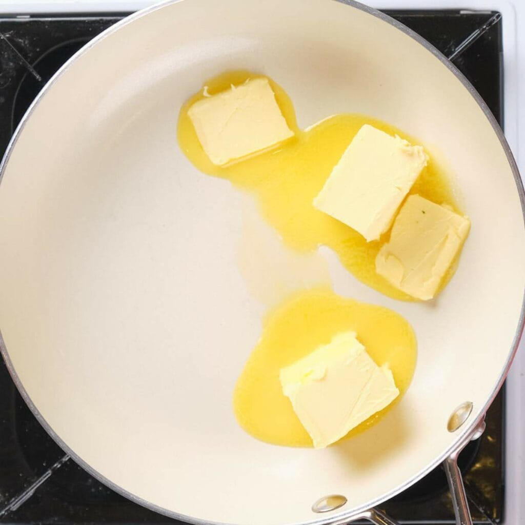 Butter melting in a white frying pan on a stovetop.