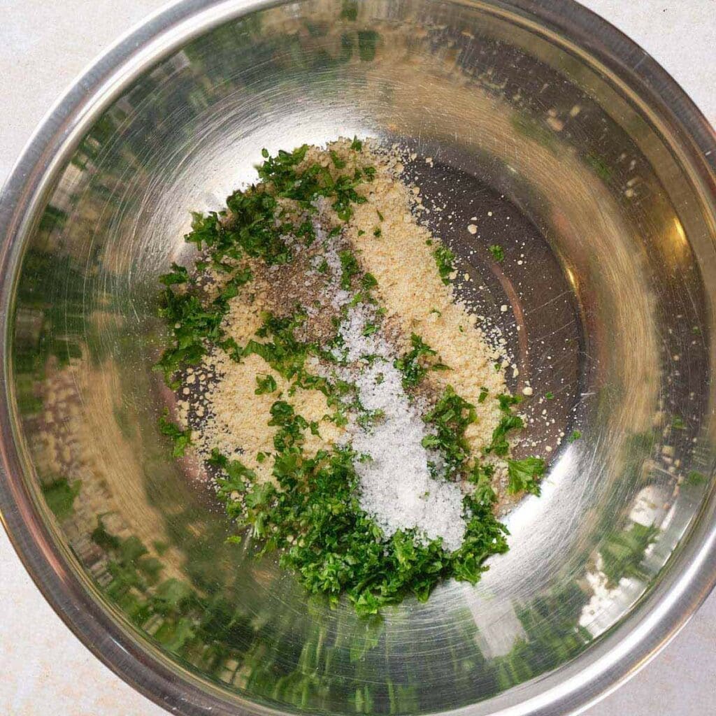 Metal bowl with chopped herbs, breadcrumbs, salt, and pepper.