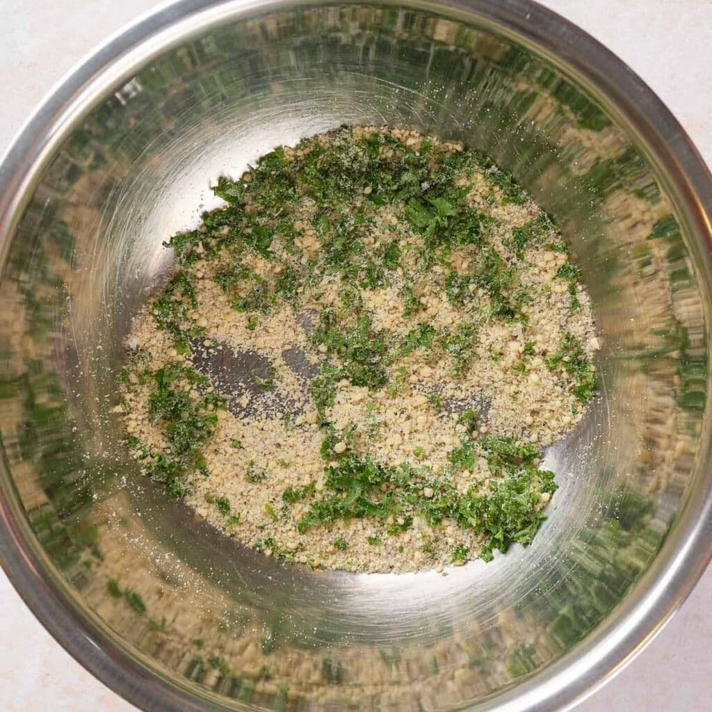 A metal bowl containing a mixture of breadcrumbs and chopped green herbs.